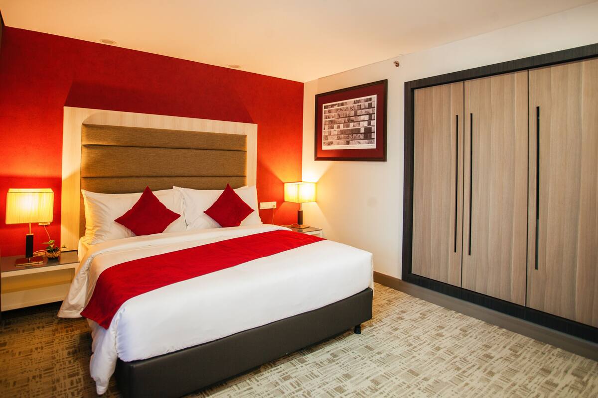 Ein Hotelzimmer mit einem großen Bett, roter und weißer Bettwäsche, zwei Nachttischlampen, einem Holzschrank und einem gerahmten Foto an der Wand.
