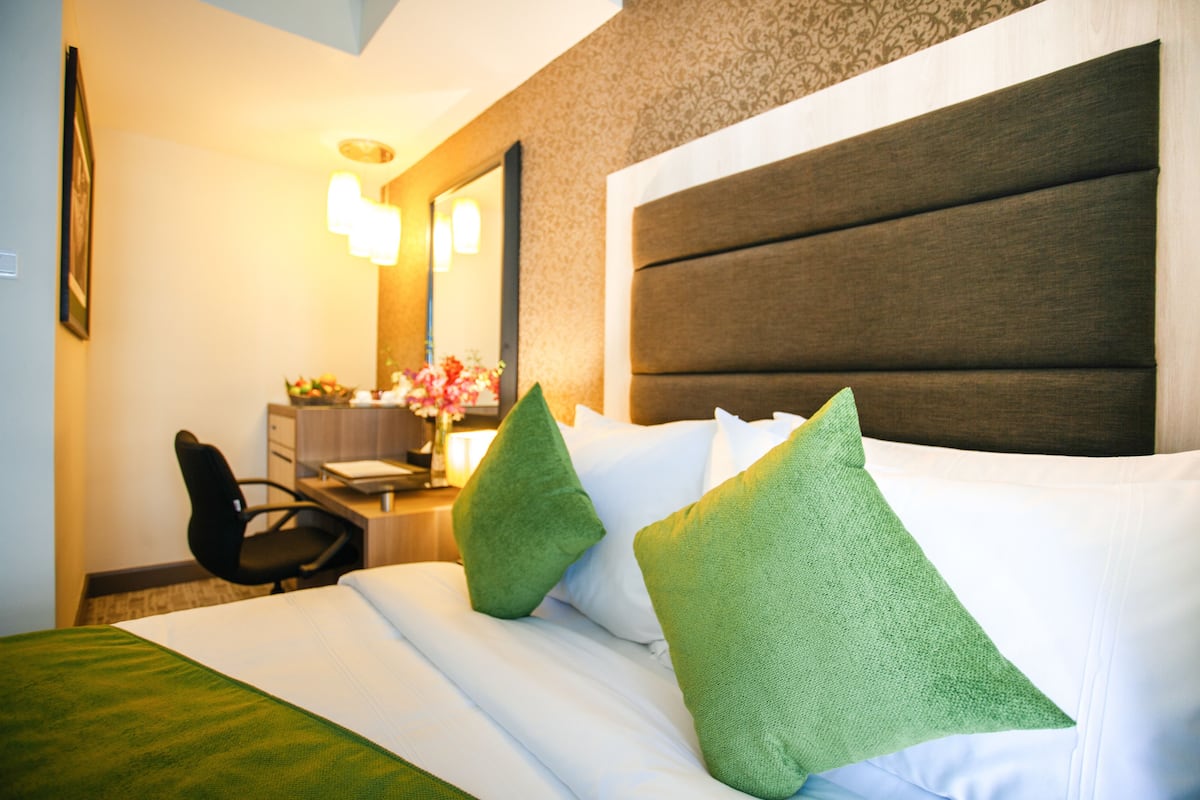 Ein Hotelzimmer mit einem großen Bett, grünen Kissen, einem Schreibtisch mit Stuhl und einem Spiegel.