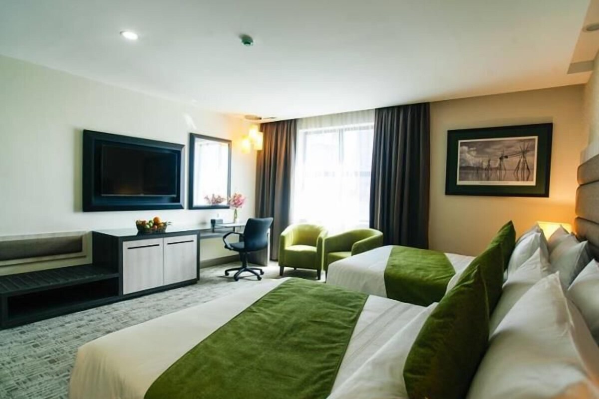 Une chambre d’hôtel avec deux lits, un bureau, une chaise, un téléviseur à écran plat et une fenêtre avec des rideaux.