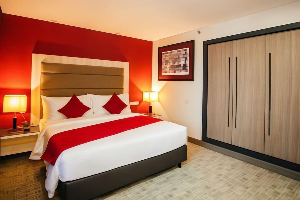 A hotel room with a large bed, two bedside lamps, a wardrobe, and a framed picture on the wall.