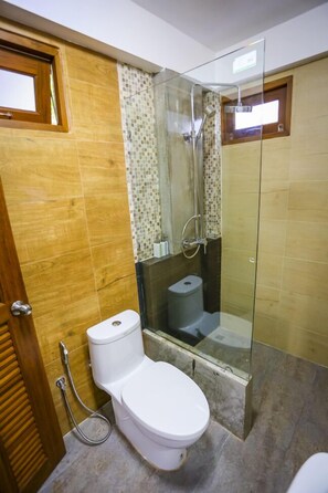 A bathroom with a toilet, a glass-enclosed shower, and a tiled wall. - Tree Home Plus Home Stay (Nakhon Si Thammarat)