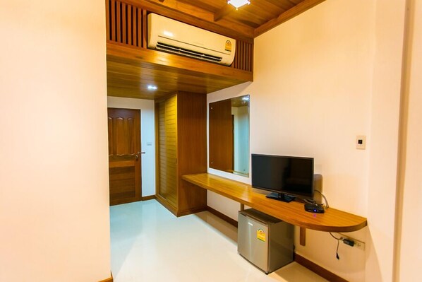 A compact room with a wooden ceiling, a built-in air conditioner, a small refrigerator, and a flat-screen TV on a wooden stand.