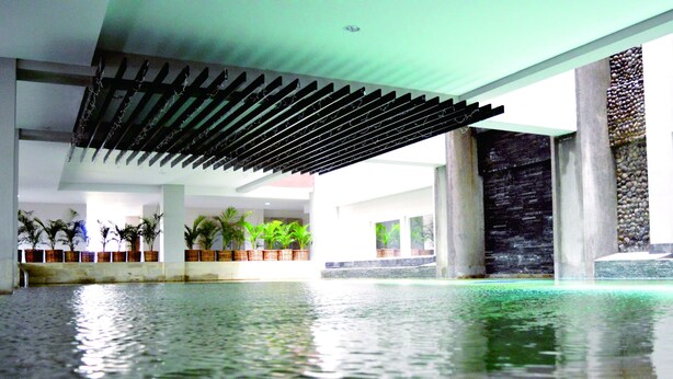 A spacious indoor pool area with a modern ceiling design, large pillars, and potted plants along the walls. - Horison Kota Lama Semarang (Semarang)