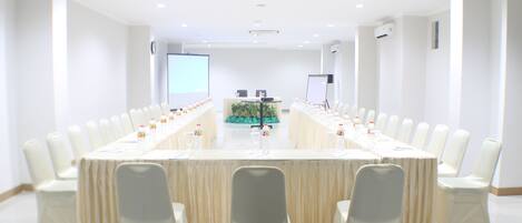 A conference room with a long table, white chairs, and a projector screen.