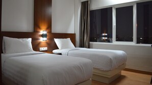 A hotel room with two beds, a nightstand with a lamp, a window with a view of the city at night, and a wooden headboard. - Horison Kota Lama Semarang (Semarang)