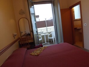 Hotellihuone, jossa on sänky, pieni pöytä, tuoli, parveke, jossa on pöytä ja tuoleja, sekä ovi, joka johtaa kylpyhuoneeseen.