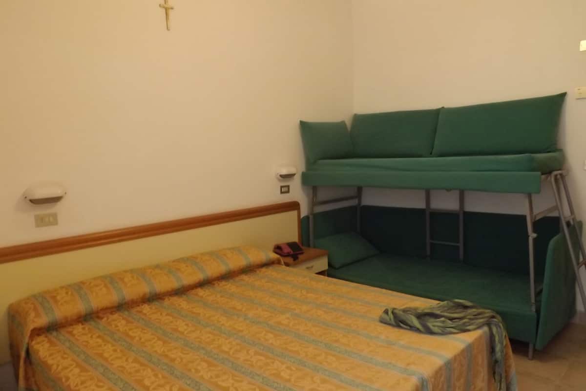 A room with a bed, a bunk bed, a bedside table, and a wall-mounted light.