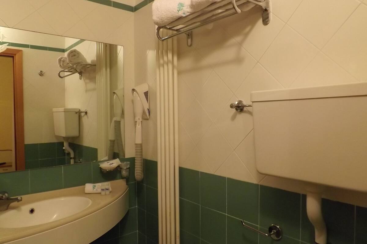 A bathroom with a sink, mirror, towel rack, toilet, and green-tiled walls.