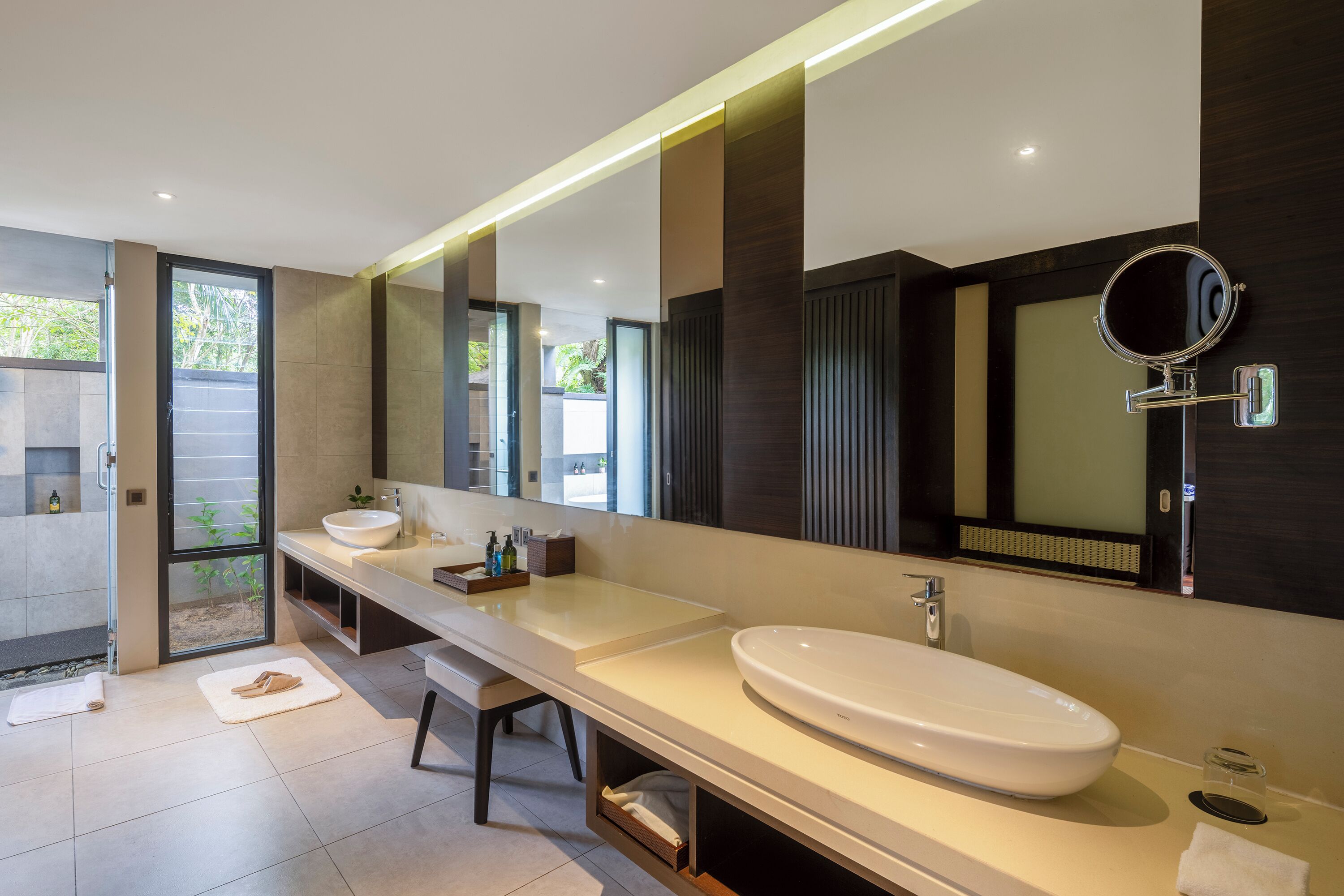 A modern bathroom with a large mirror, two sinks, and a walk-in shower.
