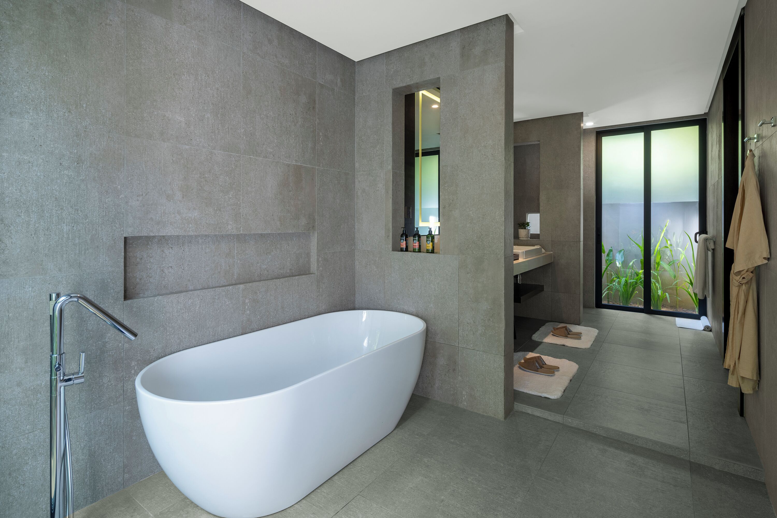 A modern bathroom with a freestanding bathtub, a large mirror, and a view of greenery outside.