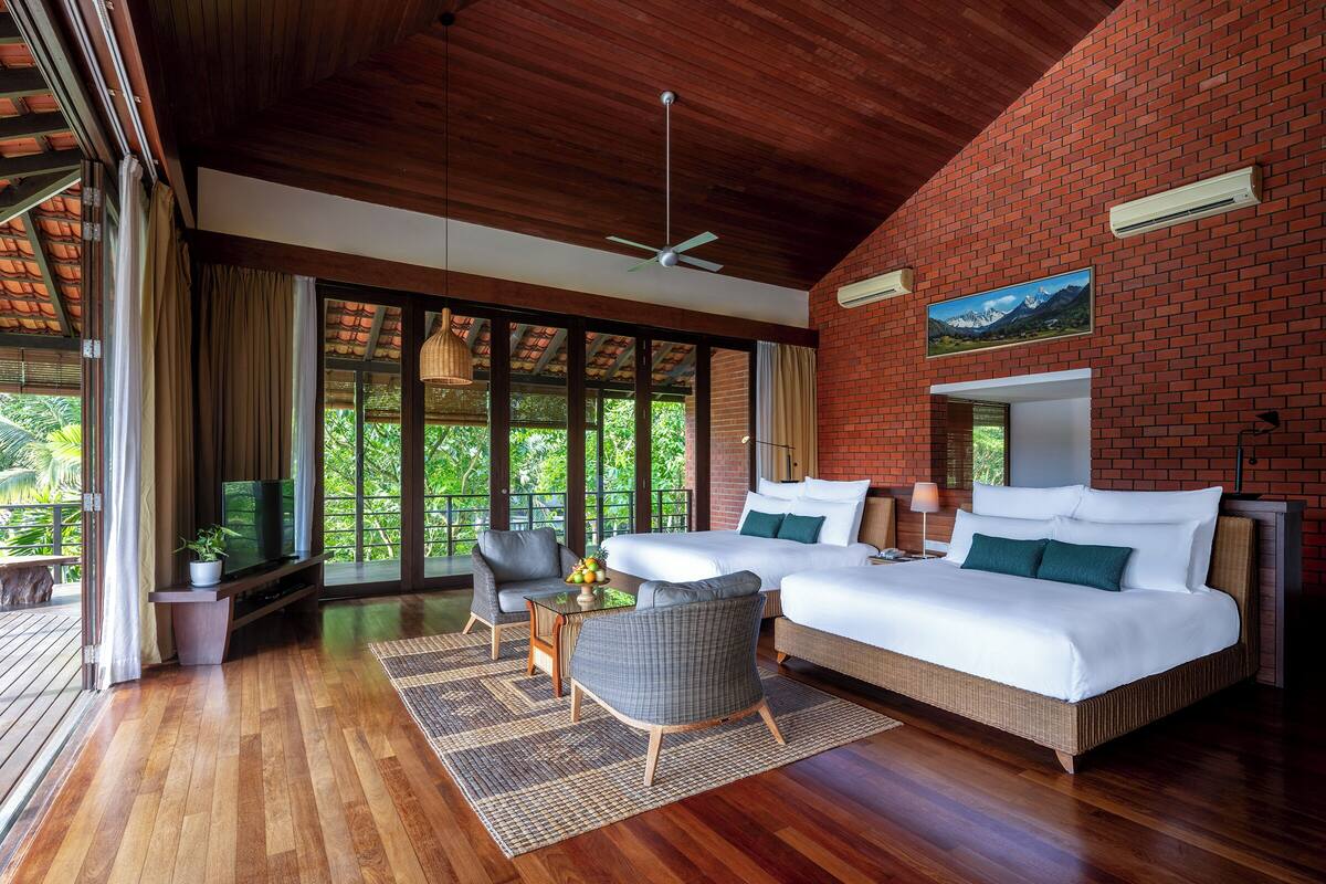Habitación amplia con una cama grande, dos sillas, televisor y balcón con vistas a zonas verdes.