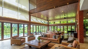 Un espace intérieur vaste et lumineux, doté de grandes fenêtres, de meubles en osier et d’un ventilateur de plafond.