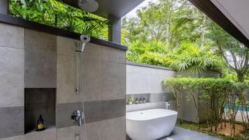 A modern bathroom with a freestanding bathtub, a shower, and a shelf with toiletries.