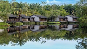 Une rangée de bungalows sur pilotis dotés de balcons, reliés par des passerelles au-dessus de l’eau, et entourés d’une végétation luxuriante.