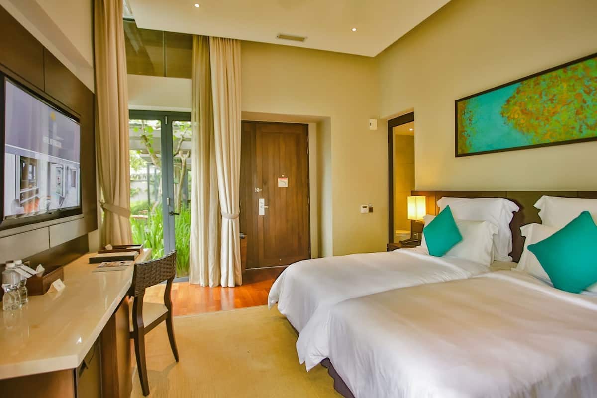 A hotel room with a bed, a desk, a TV, and a view of greenery.