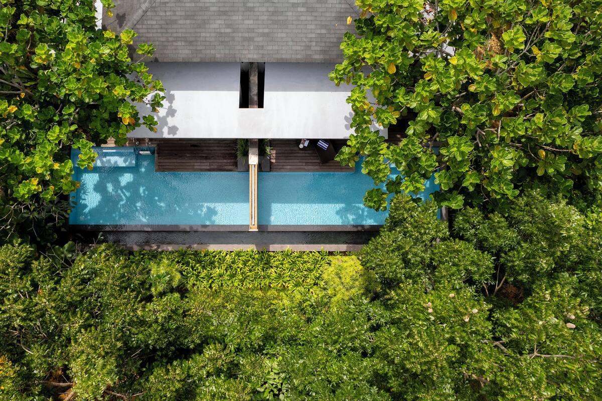 Vista aérea de una casa moderna con una piscina rectangular en el centro, rodeada de abundante follaje.