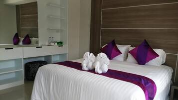 Een moderne hotelkamer met een groot bed, wit beddengoed, paarse kussens en een houten hoofdeinde.