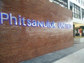 Un muro de ladrillo con el letrero iluminado 'Phitsanulok United' que indica un hotel o establecimiento similar.