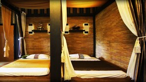 Una habitación con dos camas, suelo de madera, paredes de ladrillo y cortinas atadas en las esquinas.