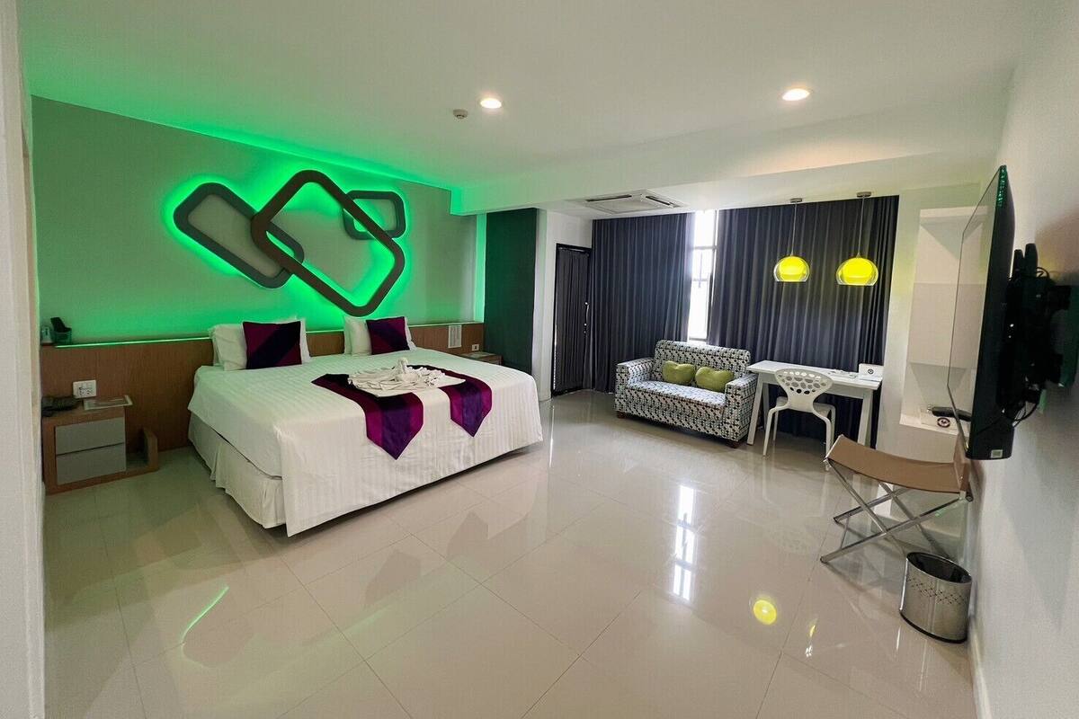 A modern hotel room with a large bed, a sofa, a desk, and a TV.