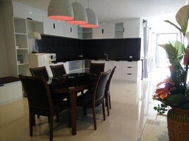 Una cocina moderna con salpicadero negro, armarios blancos y una zona de comedor con una mesa y sillas de madera oscura.