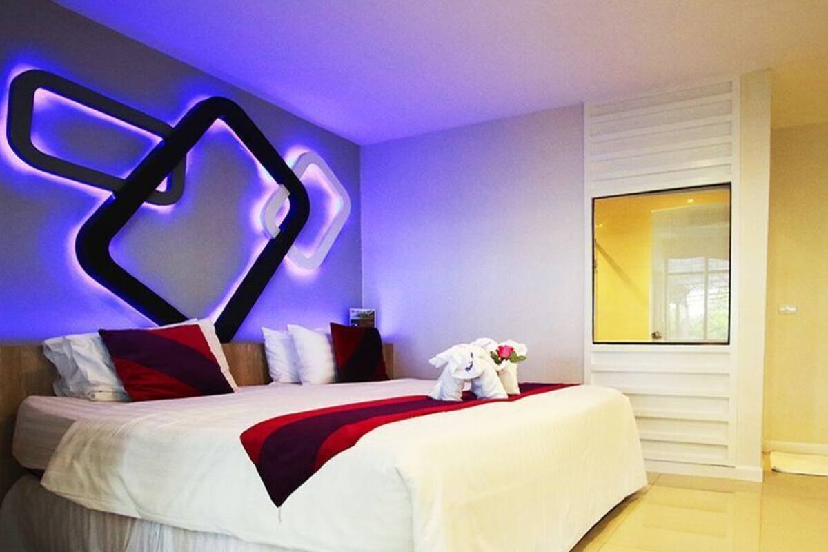A modern hotel room with a bed, a wall art piece, a window, and a door.