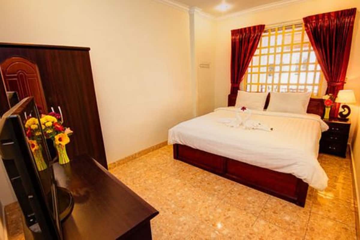 A hotel room with a bed, a wooden desk, a TV, and a window with curtains.