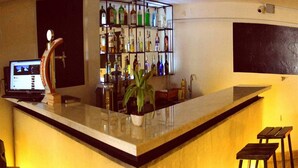 Eine Bar mit einer langen Theke, Regalen voller Flaschen, einem Laptop und einem Blumentopf.