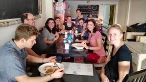 Eine Gruppe von Personen sitzt an einem Tisch in einem Raum mit einer Tafelwand, einem Esstisch und Stühlen.