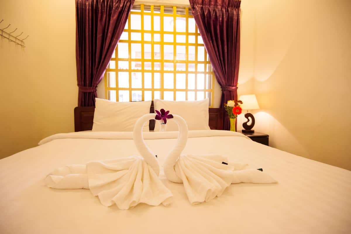 A hotel room with a bed, two swan-shaped towels, a nightstand with a lamp, and a window with curtains.