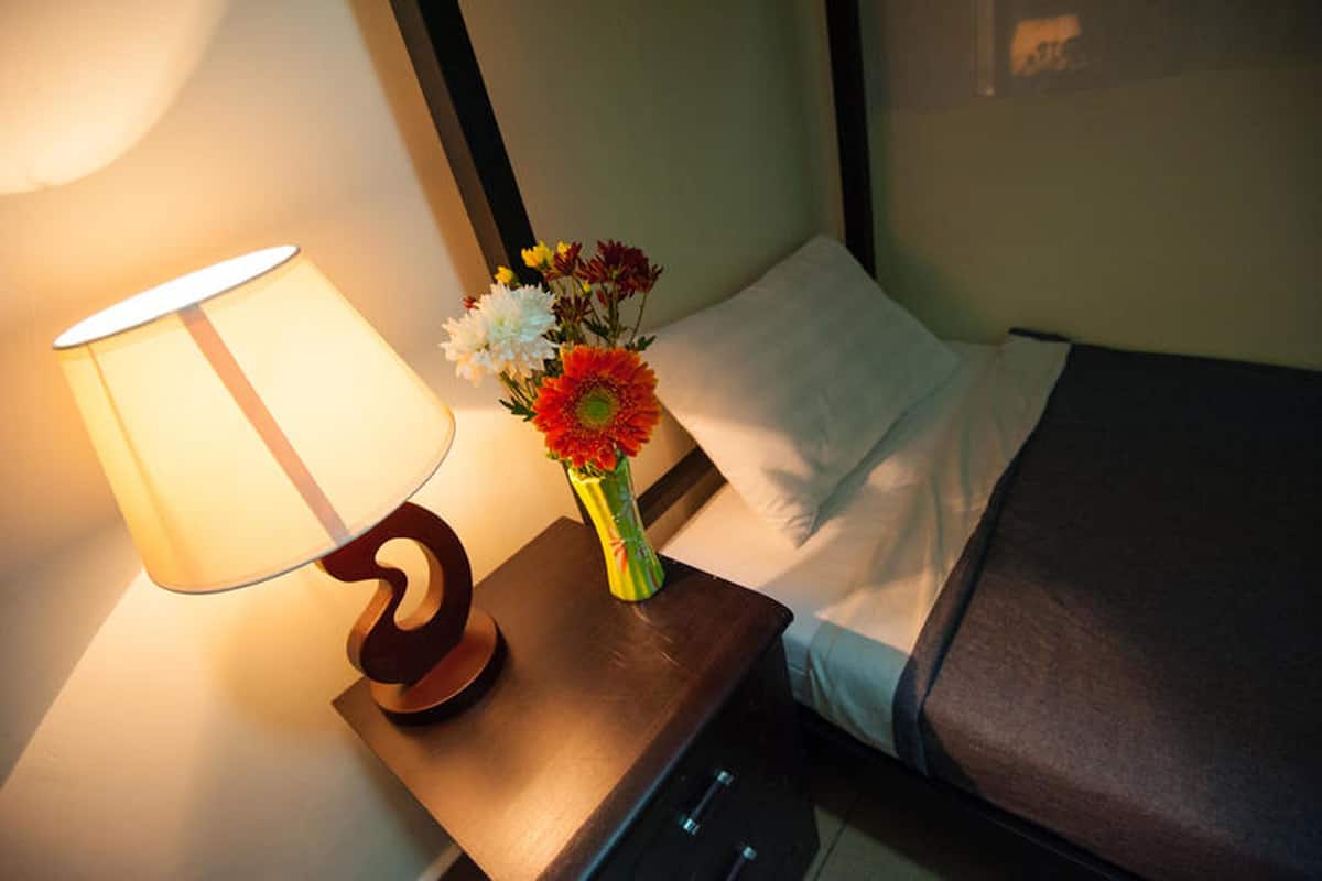 A hotel room with a bedside lamp, a vase with flowers, and a neatly made bed.