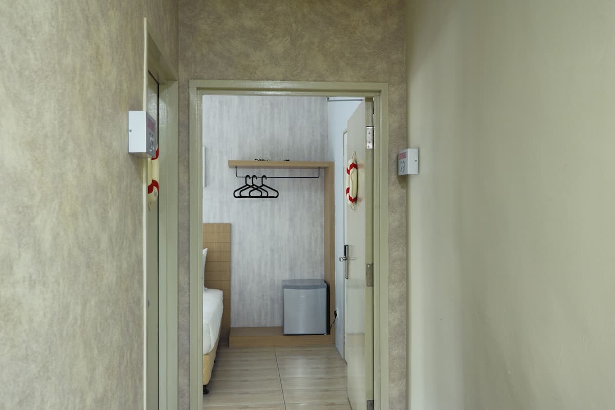 Un pasillo estrecho que conduce a una habitación con una cama, un cubo de basura pequeño y un perchero.