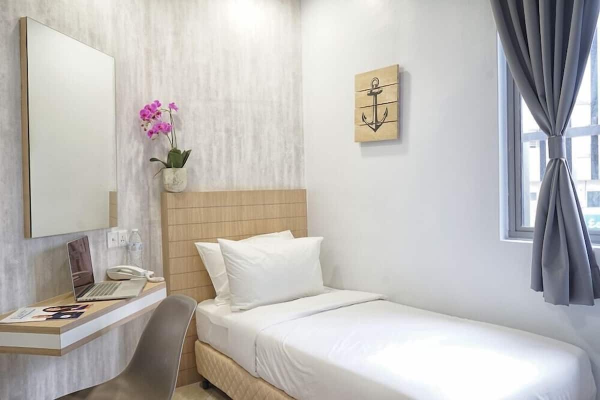 Habitación de hotel con una cama, un escritorio con una computadora portátil, un teléfono y una pequeña planta en maceta.