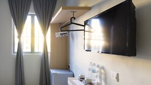 Una habitación pequeña y moderna con escritorio, televisor de pantalla plana en la pared, un refrigerador pequeño y una ventana con cortinas.