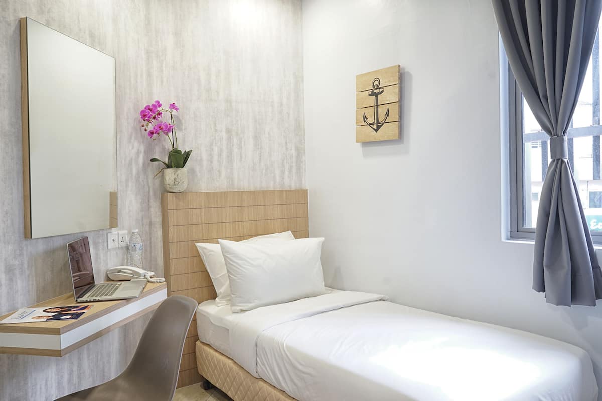 Habitación de hotel con cama, escritorio con una computadora portátil, teléfono y una pequeña orquídea en maceta.
