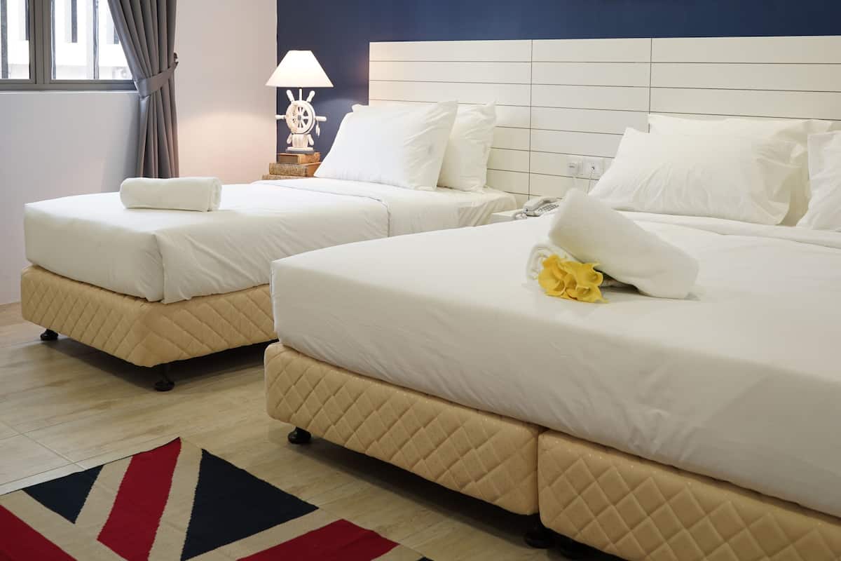 Dos camas tamaño queen con ropa de cama blanca, un tapete con el diseño de la bandera Union Jack rojo y azul, y una lámpara con forma de timón en una mesita de noche.