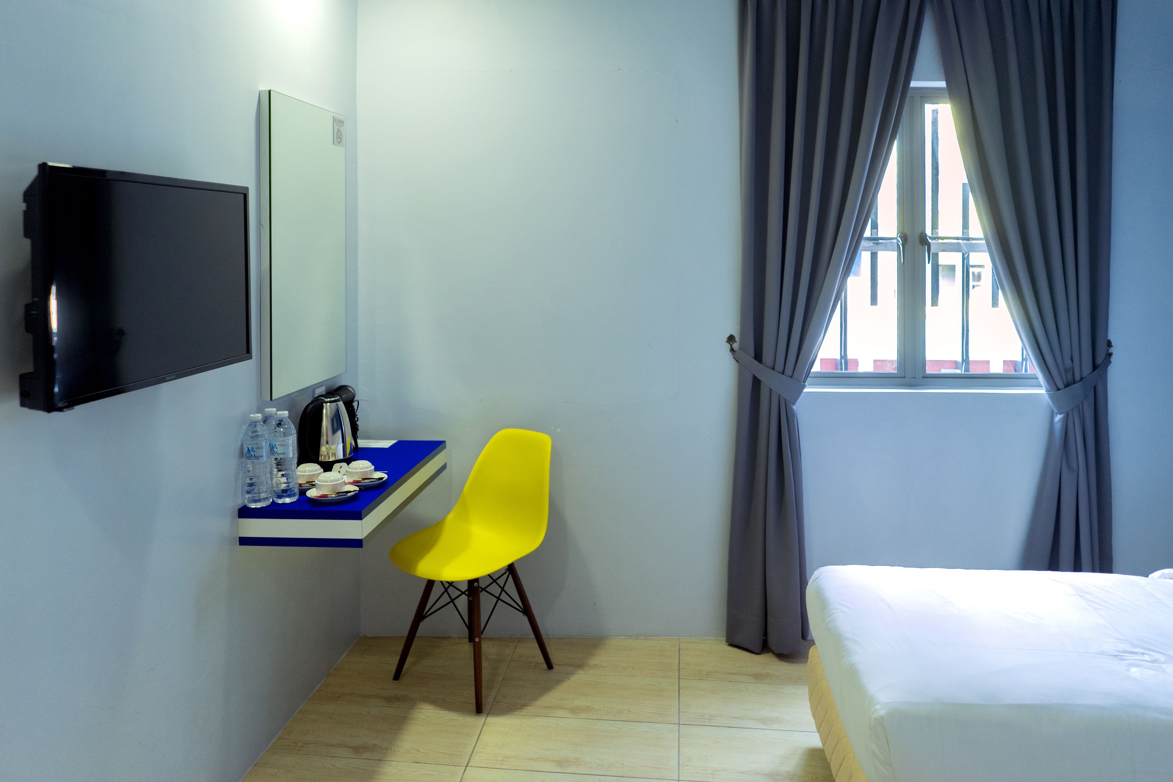 A hotel room with a bed, a desk with a chair, a TV, and a window with curtains.