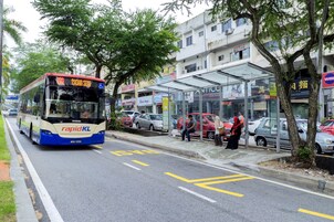 A bus with 'rapid KL' on the front, parked at a bus stop with people waiting.