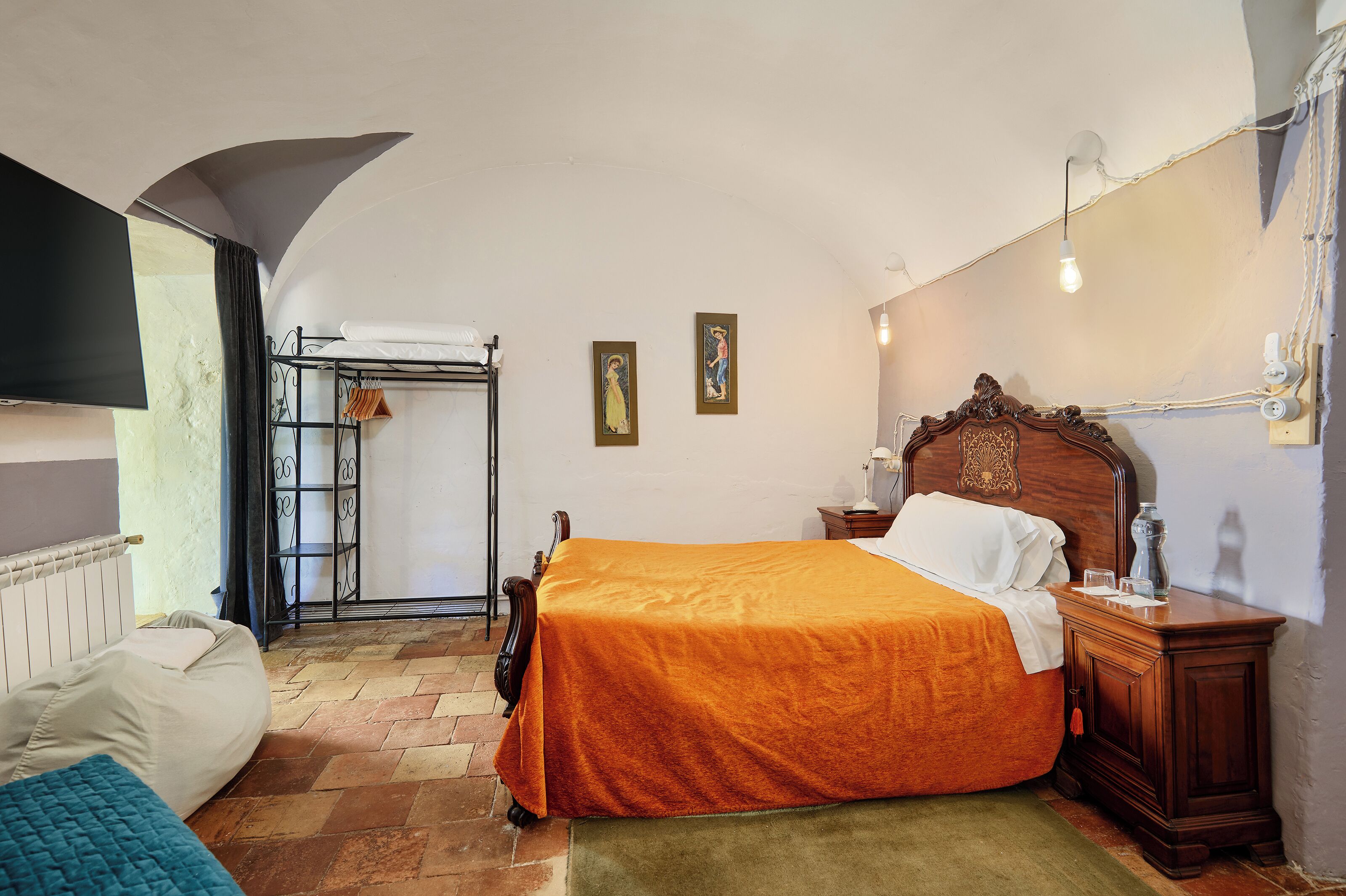 Un dormitorio con una cama, una mesita de noche de madera, un radiador, una ventana con cortinas y una lámpara de pared.