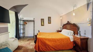 Un dormitorio con una cama, una mesita de noche de madera, un radiador, una ventana con cortinas y una lámpara de pared.
