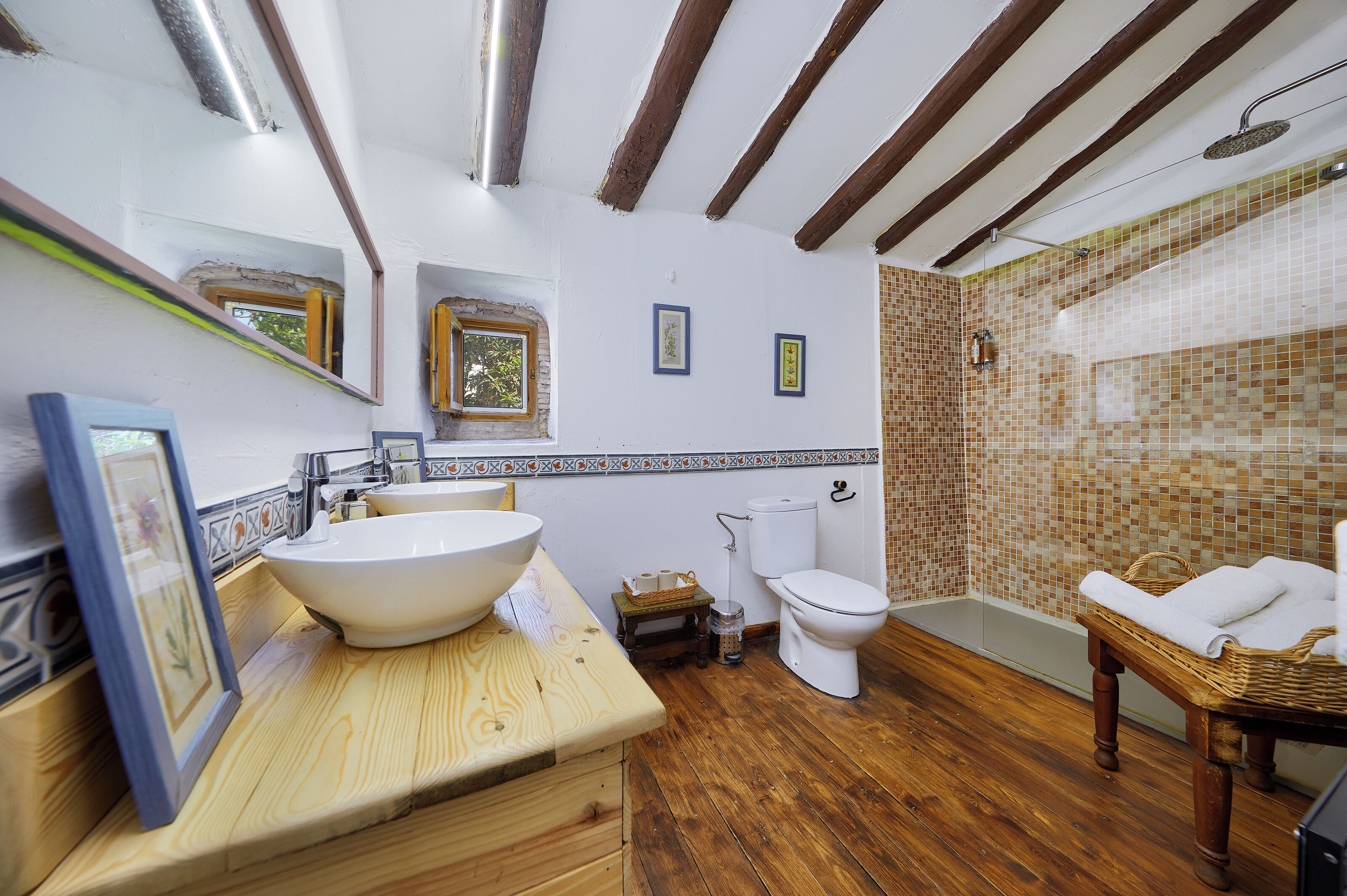A bathroom with a wooden vanity, a large sink, a toilet, and a bathtub with a wicker chair.