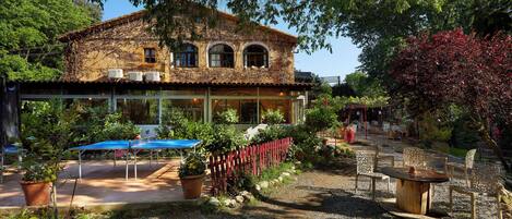 Un edificio rústico con un patio jardín, mesas al aire libre y una pérgola.