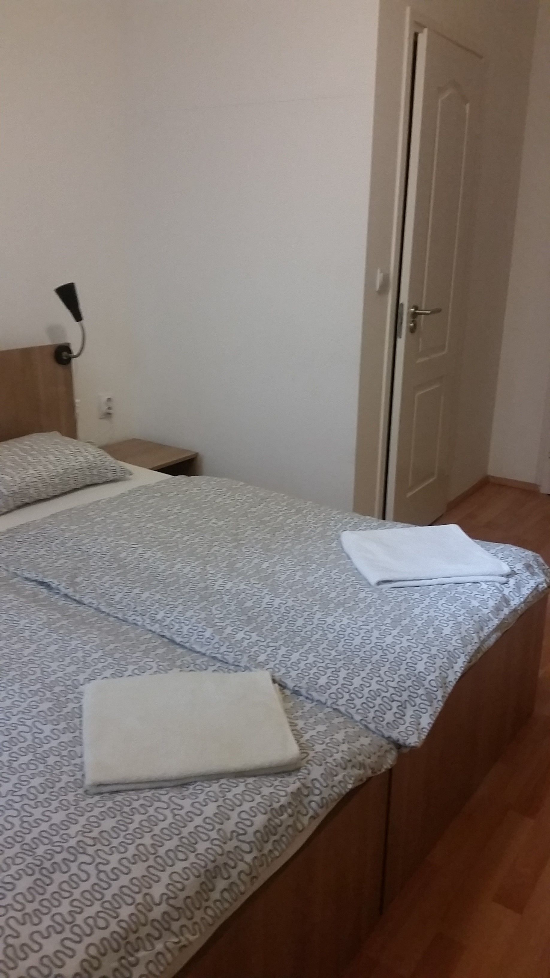 A bedroom with a bed, a nightstand, a lamp, and a door.