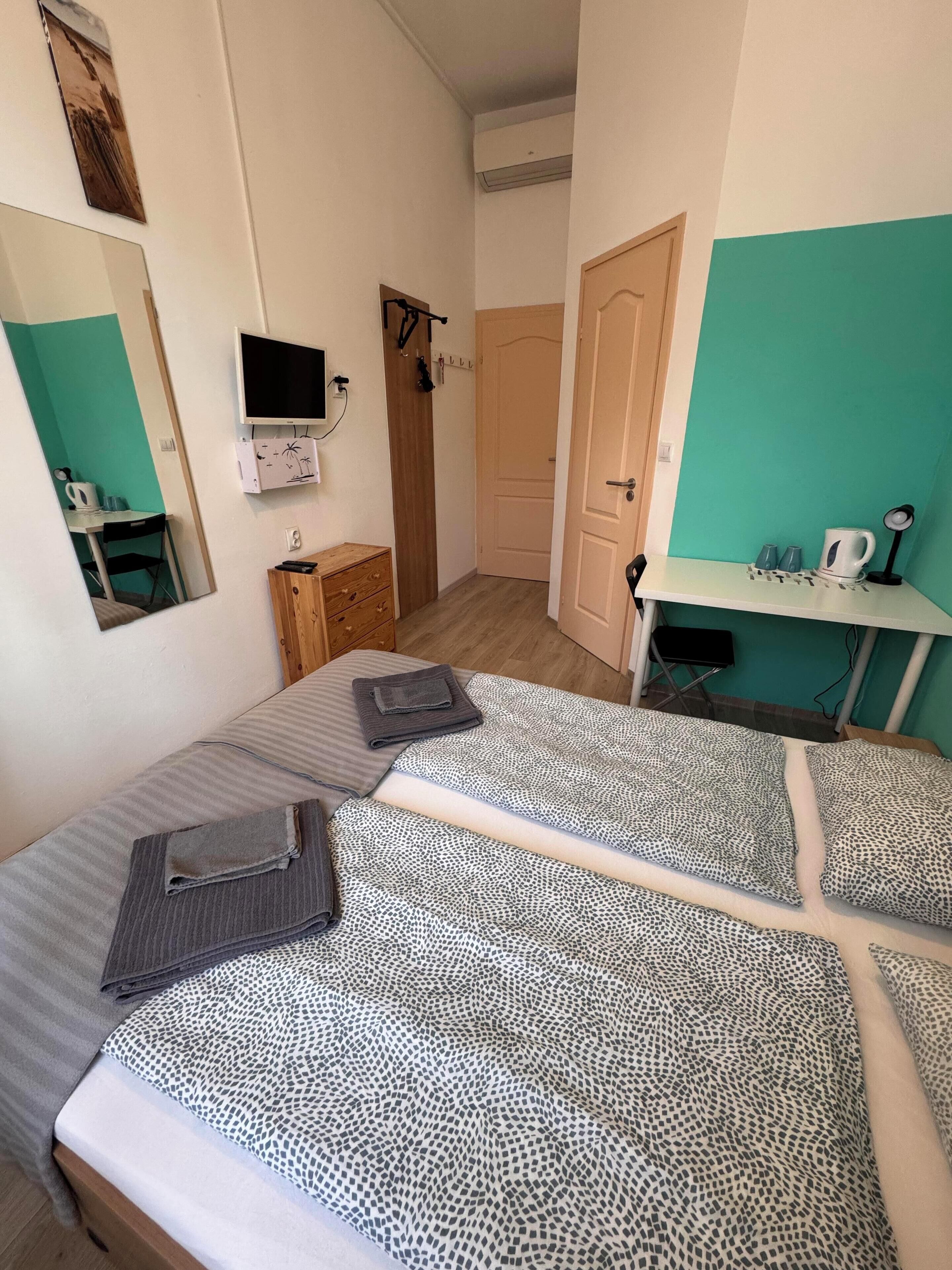 A room with two beds, a desk, a mirror, a TV, and a door.