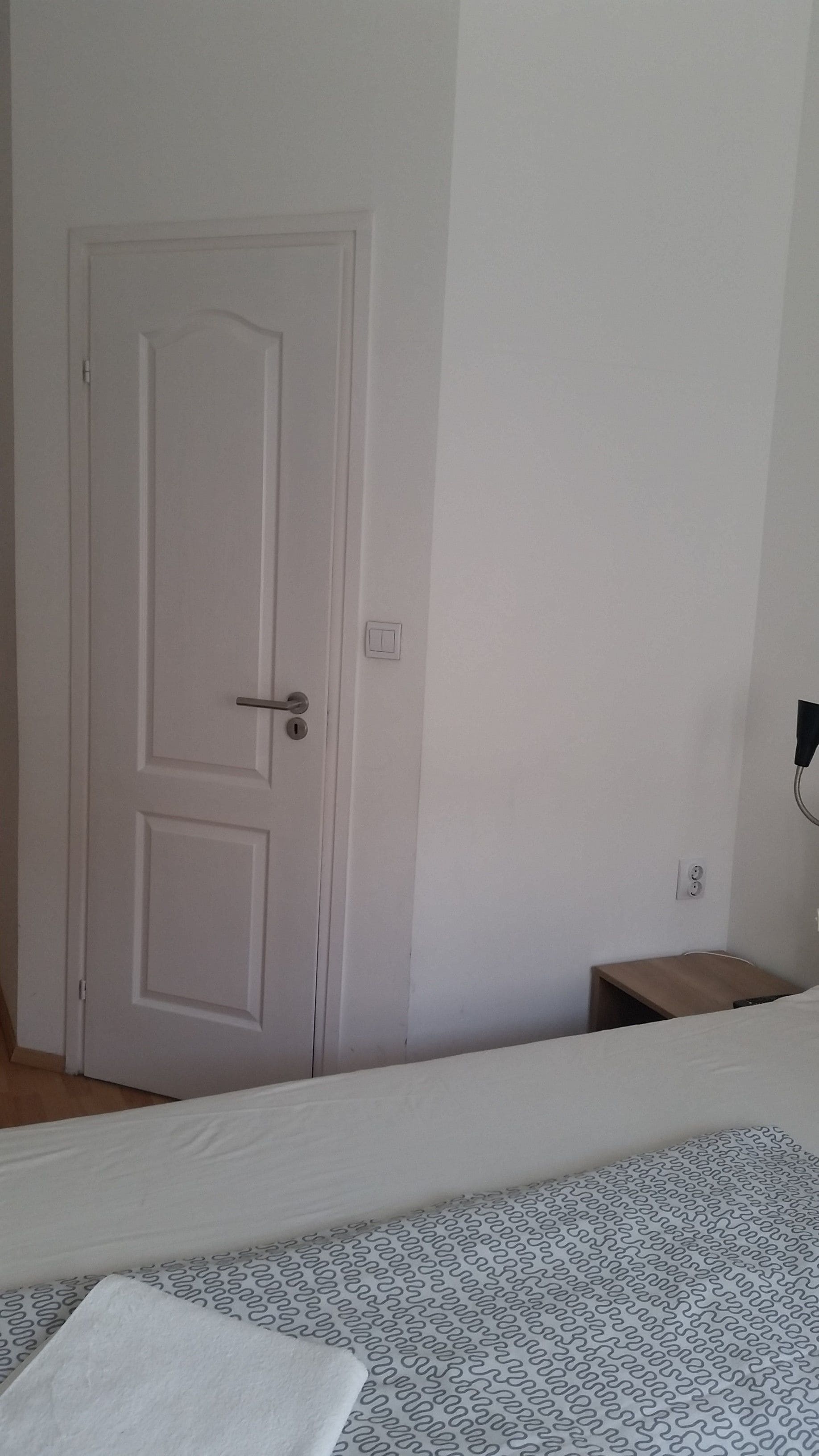 Una habitación con la puerta cerrada, una mesita de noche y una cama con colcha estampada.