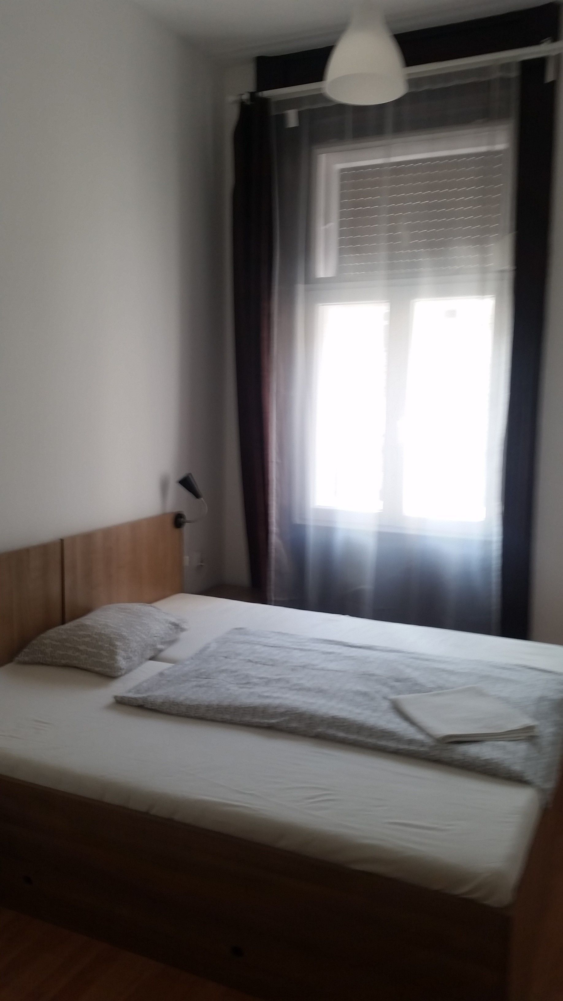 Ein Schlafzimmer mit einem Bett, einer Nachttischlampe, einem Fenster mit Vorhängen und einer Deckenleuchte.