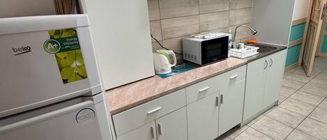 A kitchen with white cabinets, a microwave, a kettle, and a refrigerator.