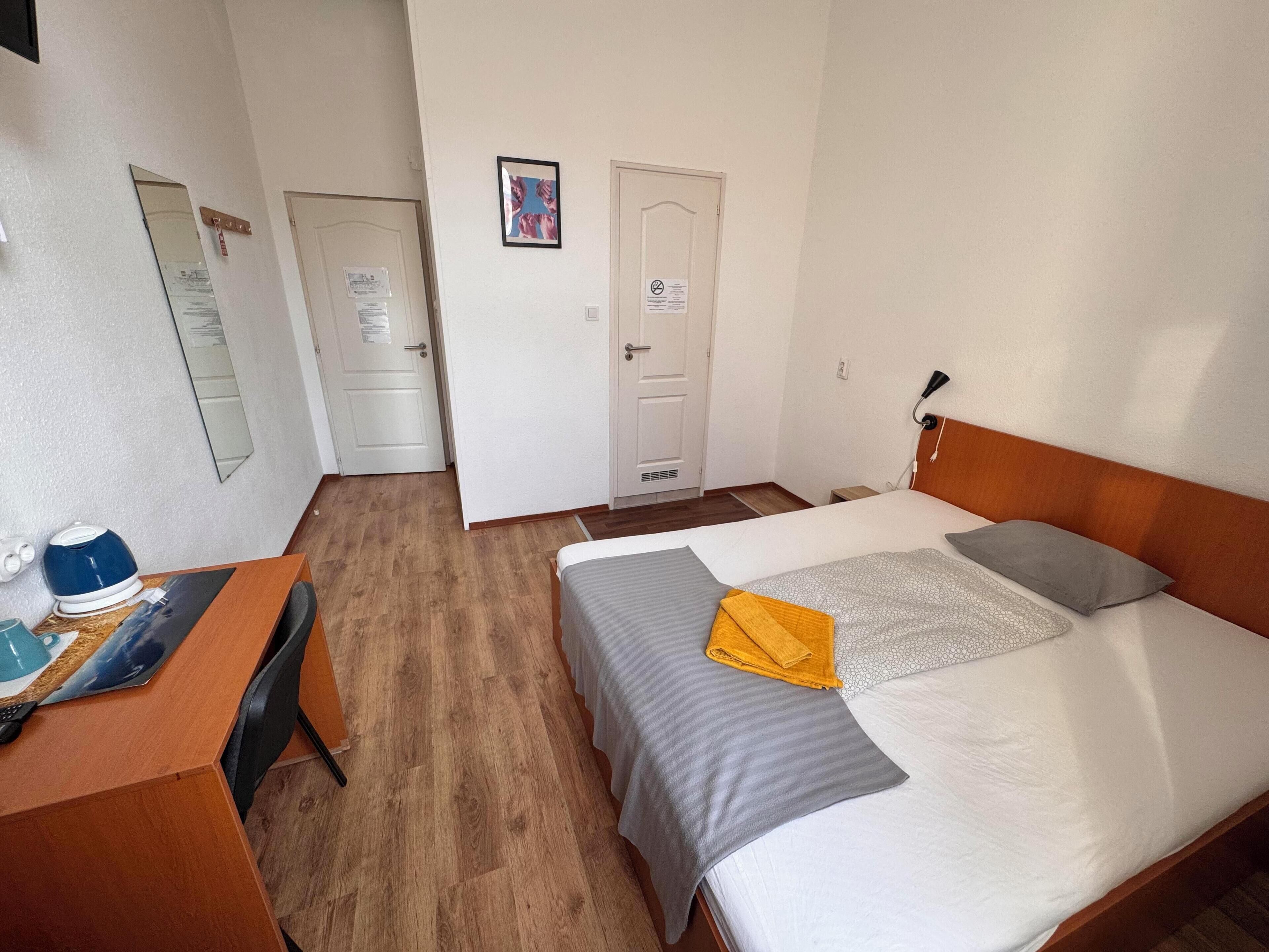 Ein Hotelzimmer mit Bett, Schreibtisch, Stuhl, Spiegel und Tür.