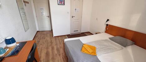 Habitación de hotel con una cama, un escritorio, una silla, un espejo y una puerta.