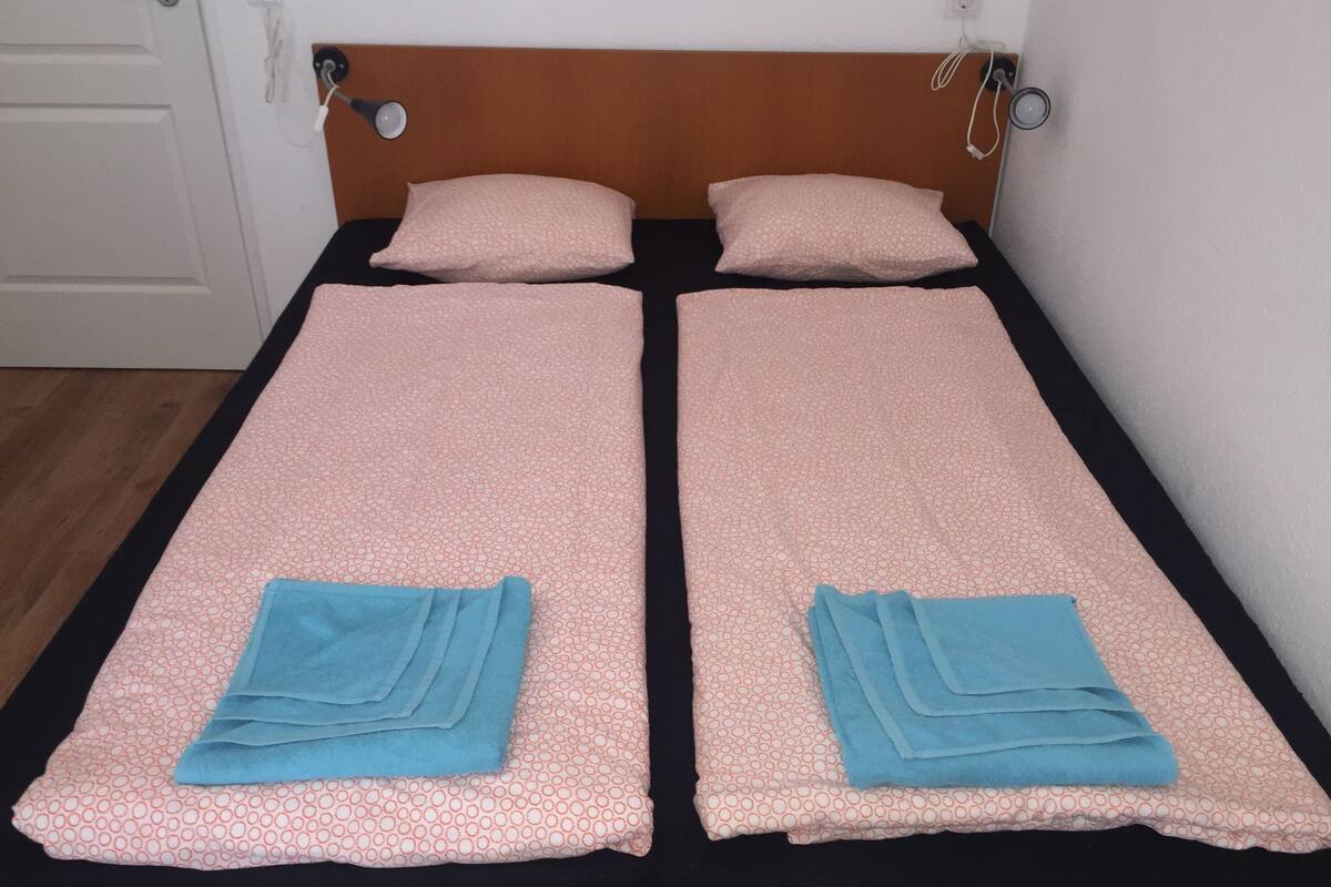 Un lit simple avec une tête de lit en bois, deux oreillers et deux serviettes bleues pliées.